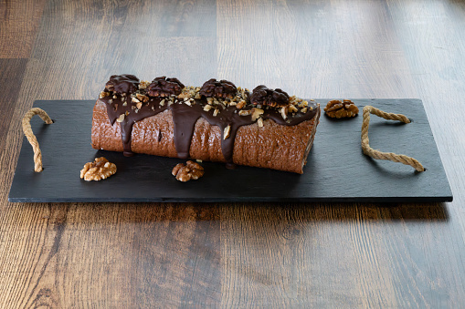 On a wooden board, a Swiss roll with hazelnuts, buttercream filling, and dark chocolate topping. This is perfect for any day or New Year's treats.