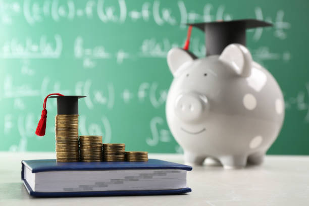 istock Scholarship concept. Coins, graduation cap and book on light grey table, space for text 1820760097