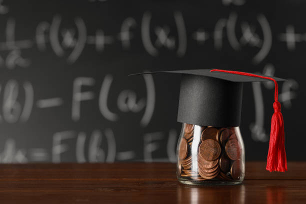 istock Scholarship concept. Graduation cap and jar with coins on wooden table, space for text 1820760607