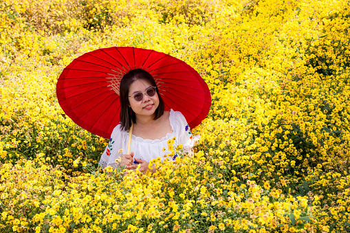 Asian woman wears white dress, happiness in yellow flower garden.
