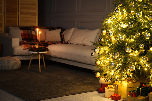Beautiful glowing Christmas tree, gift boxes and sofa in living room
