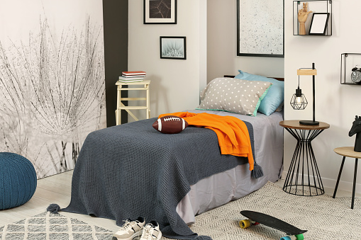 Stylish teenager's room interior with comfortable bed, lamp and football ball