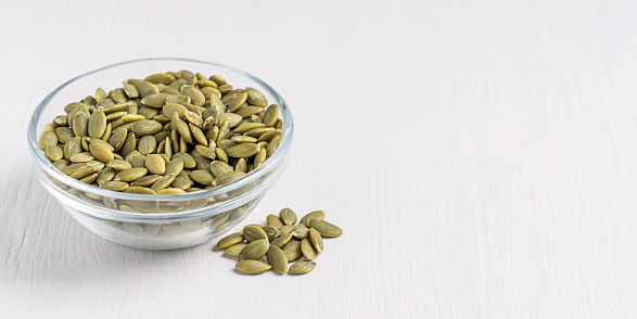 Bowl of vegetarian healthy raw dried pumpkin seeds or pepita served on white wooden background with copy space used as ingredient in cuisine and as snack with high content of fat and protein