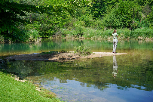 Rear view of one senior woman standing and looking  on the shore at the river against green background.