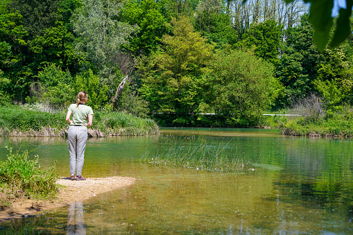 Rear view of one senior woman standing and looking  on the shore at the river against green background.