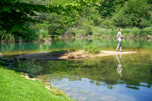 Rear view of one senior woman walking and looking  on the shore at the river against green background.