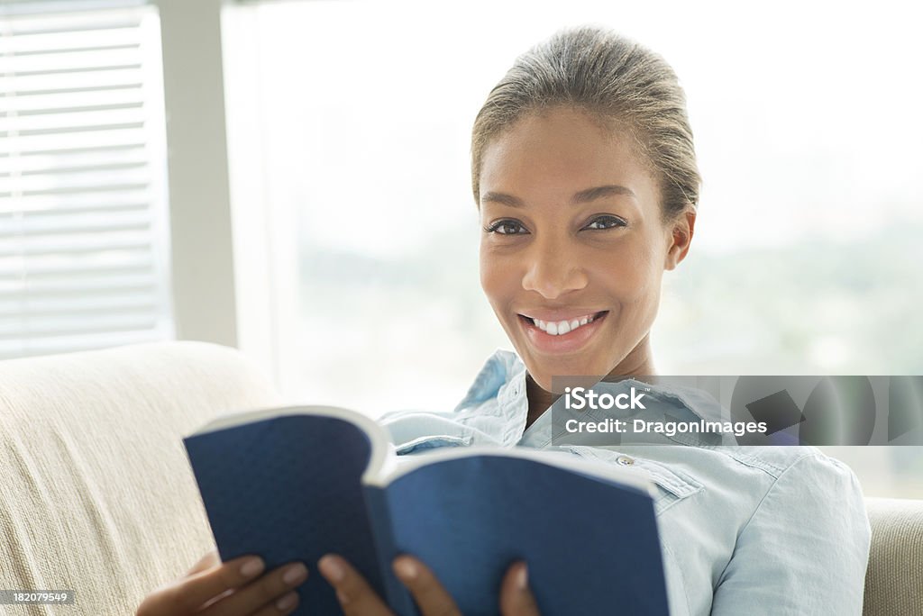 Home reading Close-up portrait of a young woman with a book on the foreground Adults Only Stock Photo