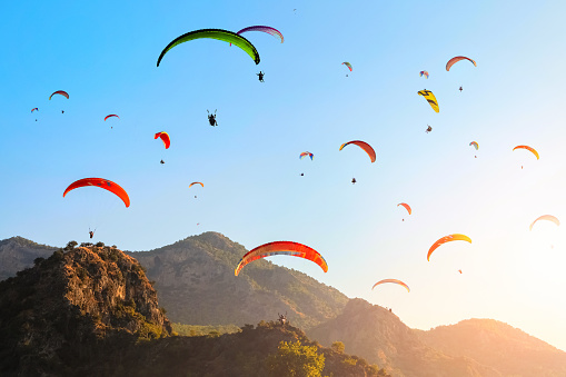 Many colorful paragliders in the blue sky over the mountains at sunset.