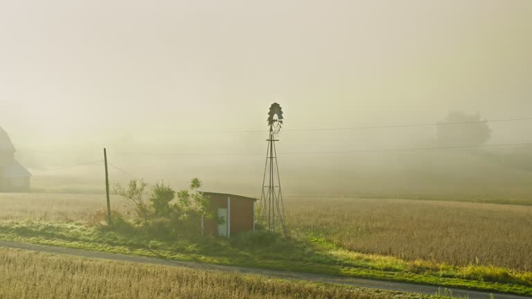 Orbiting Drone Shot of Wind Pump Surrounded by Fallow Fields on Misty Fall Morning