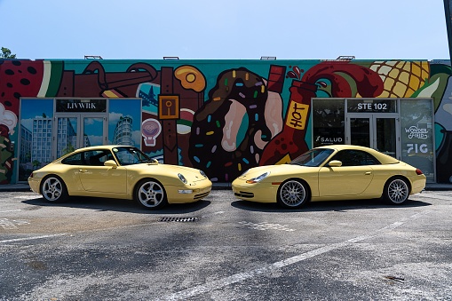 Miami, United States – November 12, 2022: Brightly colored Porsche sports cars parked near a mural in an arts district. Pastel yellow and Miami blue, in Miami, Florida.