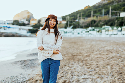 A beautiful and happy Asian woman with hat walking on a beautiful sandy beach and enjoying a beautiful day.