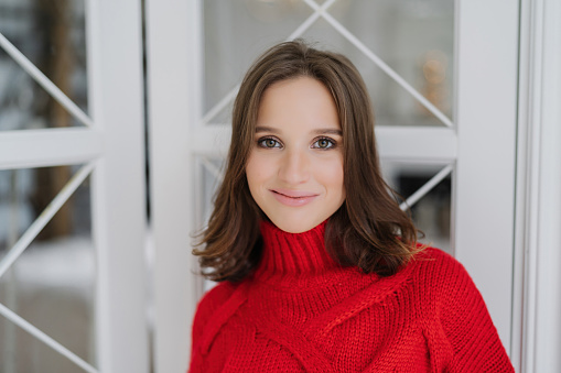 Smiling woman in a red turtleneck sweater, looking cozy and stylish, with a clear window and winter scene behind