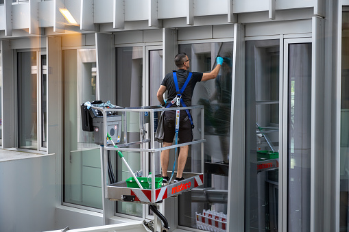 Berlin, Germany, 9/8/2023, Cleaner worker using a cherry picker to clean a glas facade of a contemporary office building