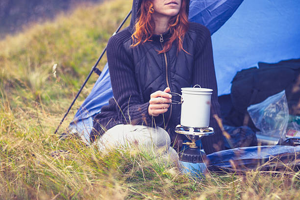A female cooking with portable gas stove while camping Young woman is sitting in her tent and cooking using a portable camping stove camping stove photos stock pictures, royalty-free photos & images