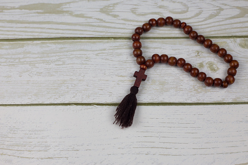 Brown wooden priest beads with the cross of Jesus Christ isolated on a white wooden table. Accessory for a believer to hold in his hands when praying to God