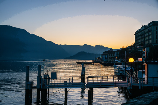 Awe Evening sunset view on lake Como and some boats anchore and buildings pon coast (hotel?)., pier and electric light. Short trip during Christmas week,