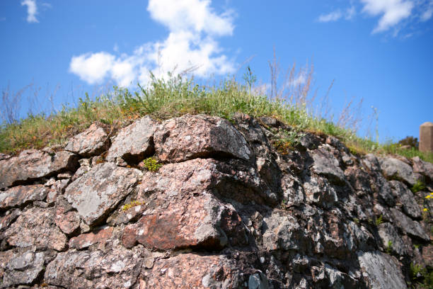 Close-up of an corner ancient red granite stone brick wall, blue clean sky, green grass