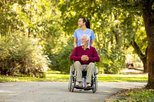 istock Nursing assistant and elderly man in wheelchair going for a walk in the park. 1820902629