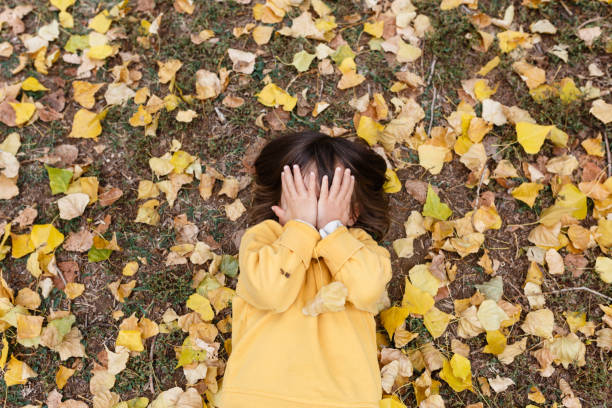 istock upper view on little girl hiding face with hands lying between yellow leaves 1820907688