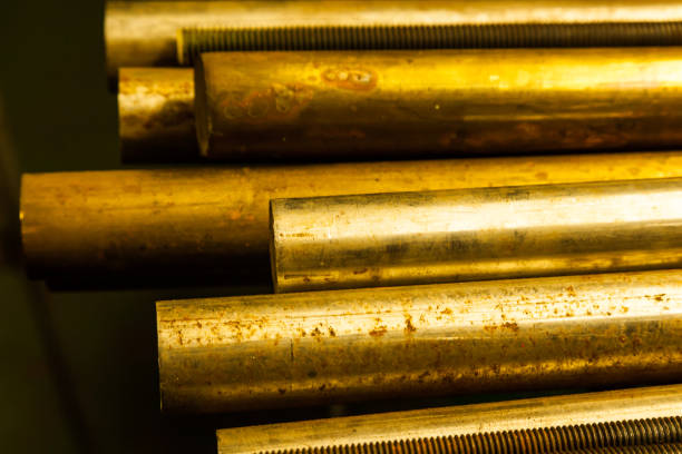 Large bronze round bars and steel threaded rods lie on a shelf, close-up.