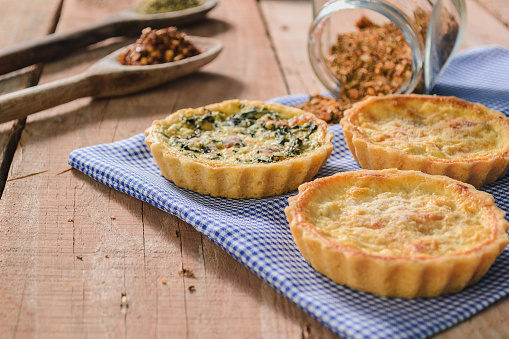 An irresistible display of cheese and leek quiches, delicately arranged on a rustic wooden table. Each quiche, a golden and delicious masterpiece, is adorned with the savory touch of leeks, providing an explosion of harmonious flavors