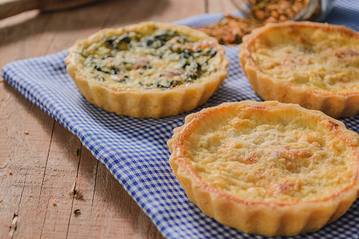 An irresistible display of cheese and leek quiches, delicately arranged on a rustic wooden table. Each quiche, a golden and delicious masterpiece, is adorned with the savory touch of leeks, providing an explosion of harmonious flavors