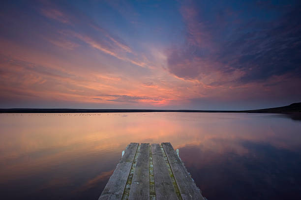 jetty lake sunset in yorkshire A sailing club jetty pointing directly towards a pastel coloured sunset reflected in the still waters of a moorland reservoir. burton sussex stock pictures, royalty-free photos & images
