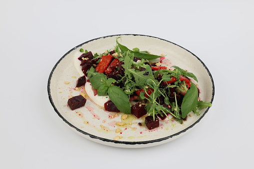 Baked beetroot salad with cheese and greens on a beautiful white plate on a white background.