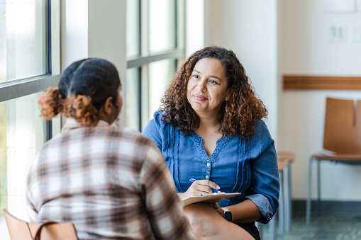 An unrecognizable young adult female college student shares her struggles with the cheerful mid adult female counselor.