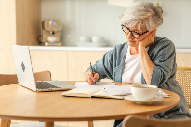 istock Online education courses webinar concept. Middle aged senior woman using laptop computer writing notes. Focused mature old woman enjoying studying online from home written records doing online work. 1820948024