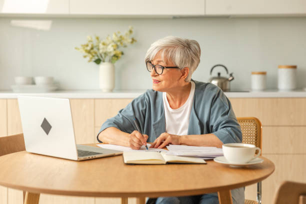 istock Online education courses webinar concept. Middle aged senior woman using laptop computer writing notes. Focused mature old woman enjoying studying online from home written records doing online work. 1820948030