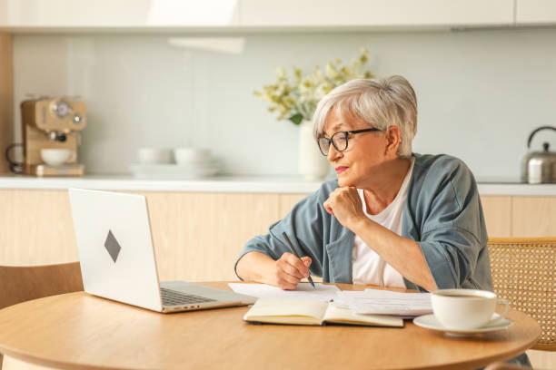 istock Online education courses webinar concept. Middle aged senior woman using laptop computer writing notes. Focused mature old woman enjoying studying online from home written records doing online work. 1820948040