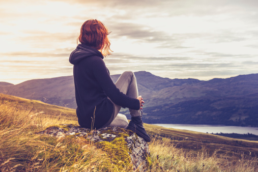 Young woman is sitting on a rock on top of a mountain and admiring the sunset