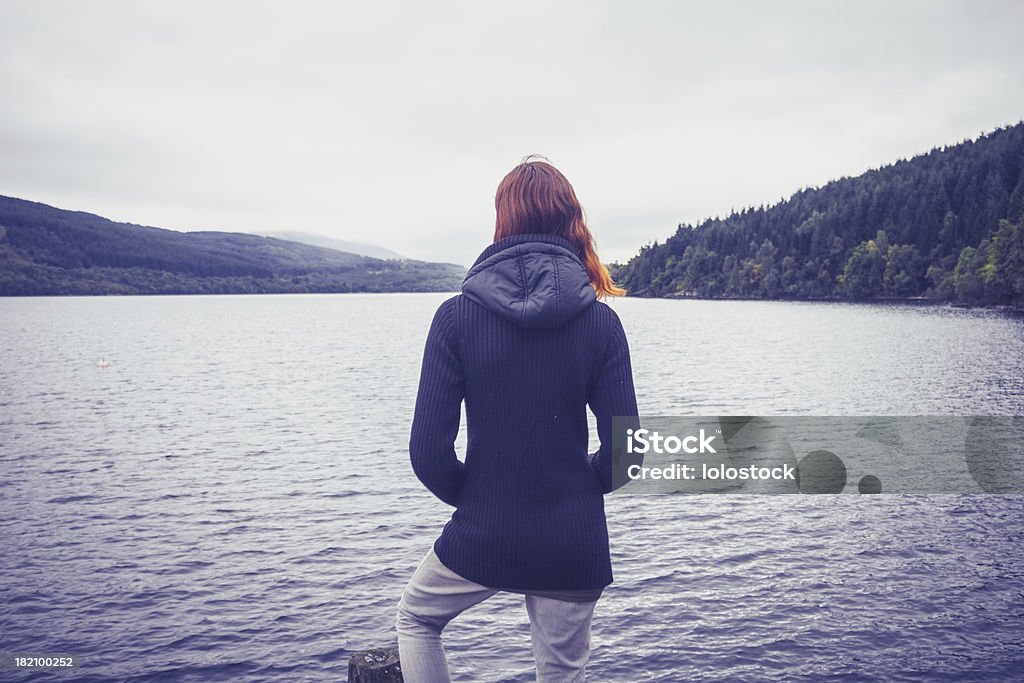 Woman admiring stillness of the lake Rear view of young woman standing at the water's edge and admiring the stillness of a lake Admiration Stock Photo