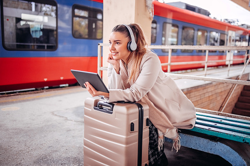 Woman waiting for train with suitcase going on vacation