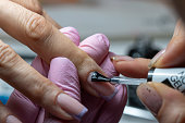 Close-up shot of a woman hand in a nail salon receiving manicure by beautician with brush.