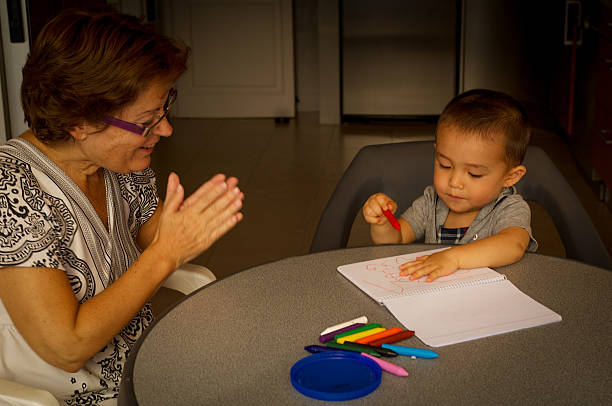 little boy is drawing with his grandmother stock photo