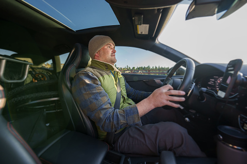 Profile view of a middle aged man with a physical disability who uses a wheelchair driving his car with adaptive technology on a sunny but chilly day in Oregon.