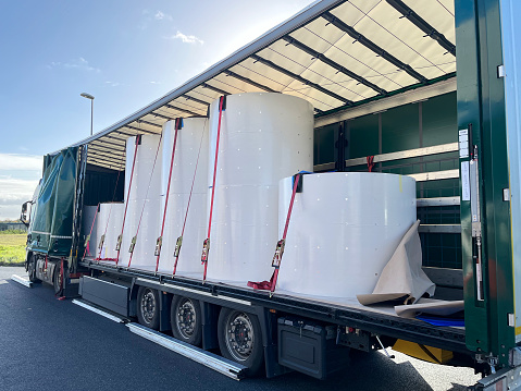 Loading, transporting and unloading large rolls of paper in a semi-trailer. Securing cargo with straps and locks for stability.