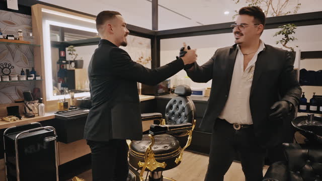 Smiling Barber and Male Client Shaking Hands and Hugging Each Other After Haircut in Barbershop