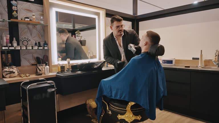 SLO MO Young Male Barber Using Blow Dryer After Cutting Customer's Hair in Salon