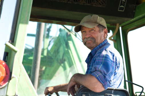 A candid portrait of a senior male farmer sitting in a green tractor.