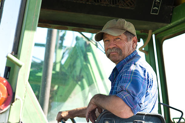 Farmer in his Tractor A candid portrait of a senior male farmer sitting in a green tractor. Farmer stock pictures, royalty-free photos & images