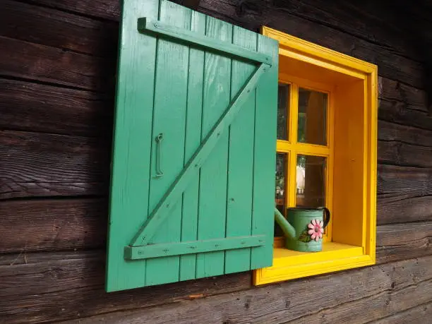 Ethno-folk wooden shutters on a window with a wooden frame, painted green and yellow. Vintage Serbian house, exterior. Architectural complex Stanisici, Bielina, Bosnia and Herzegovina. Log cabin