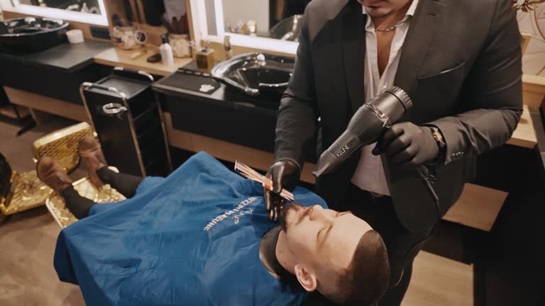 High Angle Shot of Young Male Hairdresser Using Blow Dryer After Cutting Customer's Hair in Barbershop