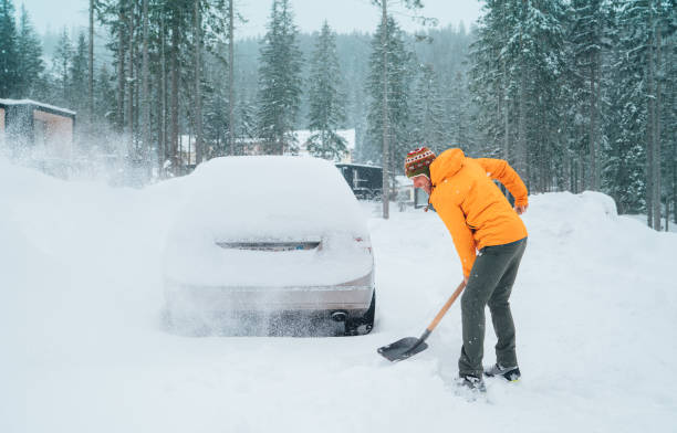 istock Smiling man with a shovel removing snow from the path and cleaning auto. Car covered with snow as a huge snowdrift on the countryside forest home driveway. Winter morning routine. 1821365713