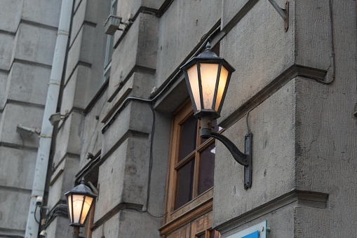 Burning street lamps in vintage style on the facade of an old town house in the city center, details and elements of architecture, interesting background, cityscape, autumn.