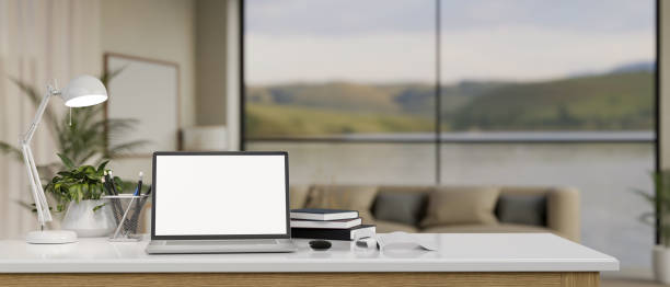 istock Close-up image of a white-screen laptop mockup on a white tabletop in a modern spacious living room. 1821424741