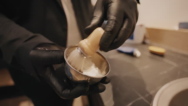 Closeup of Young Barber Mixing Shaving Cream in Bowl With Wet Brush at Barbershop