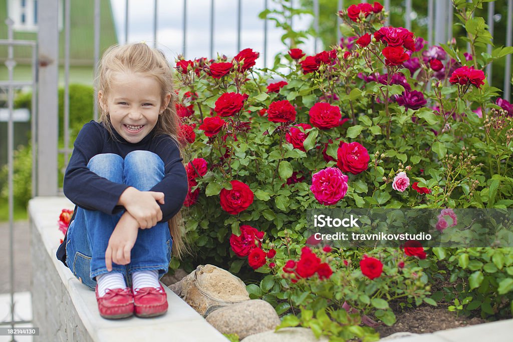 Urocza dziewczynka w pobliżu kwiaty w podwórku domu - Zbiór zdjęć royalty-free (Czerwony)